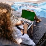 unrecognizable female remote employee working on laptop near swimming pool