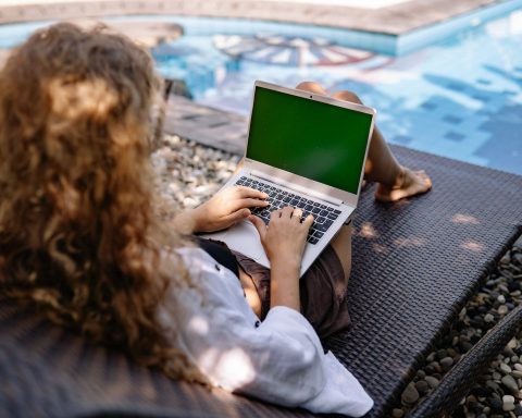 unrecognizable female remote employee working on laptop near swimming pool