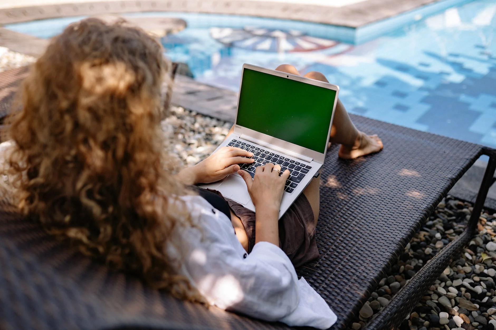 unrecognizable female remote employee working on laptop near swimming pool